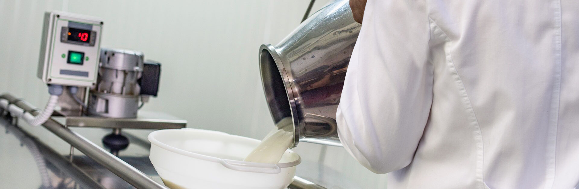 Holmen Cheese team member pouring liquid ingredient into funnel atop cheese production machine