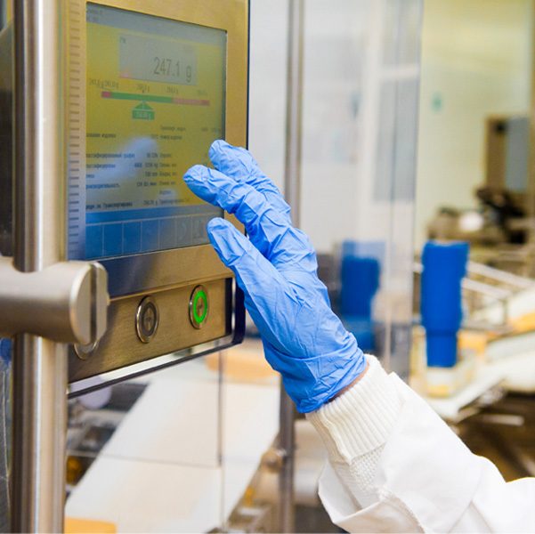 Gloved right hand and forearm of team member about to touch a touch screen on cheese production machine