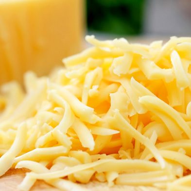 Pile of shredded yellow cheese with block of yellow cheese in background